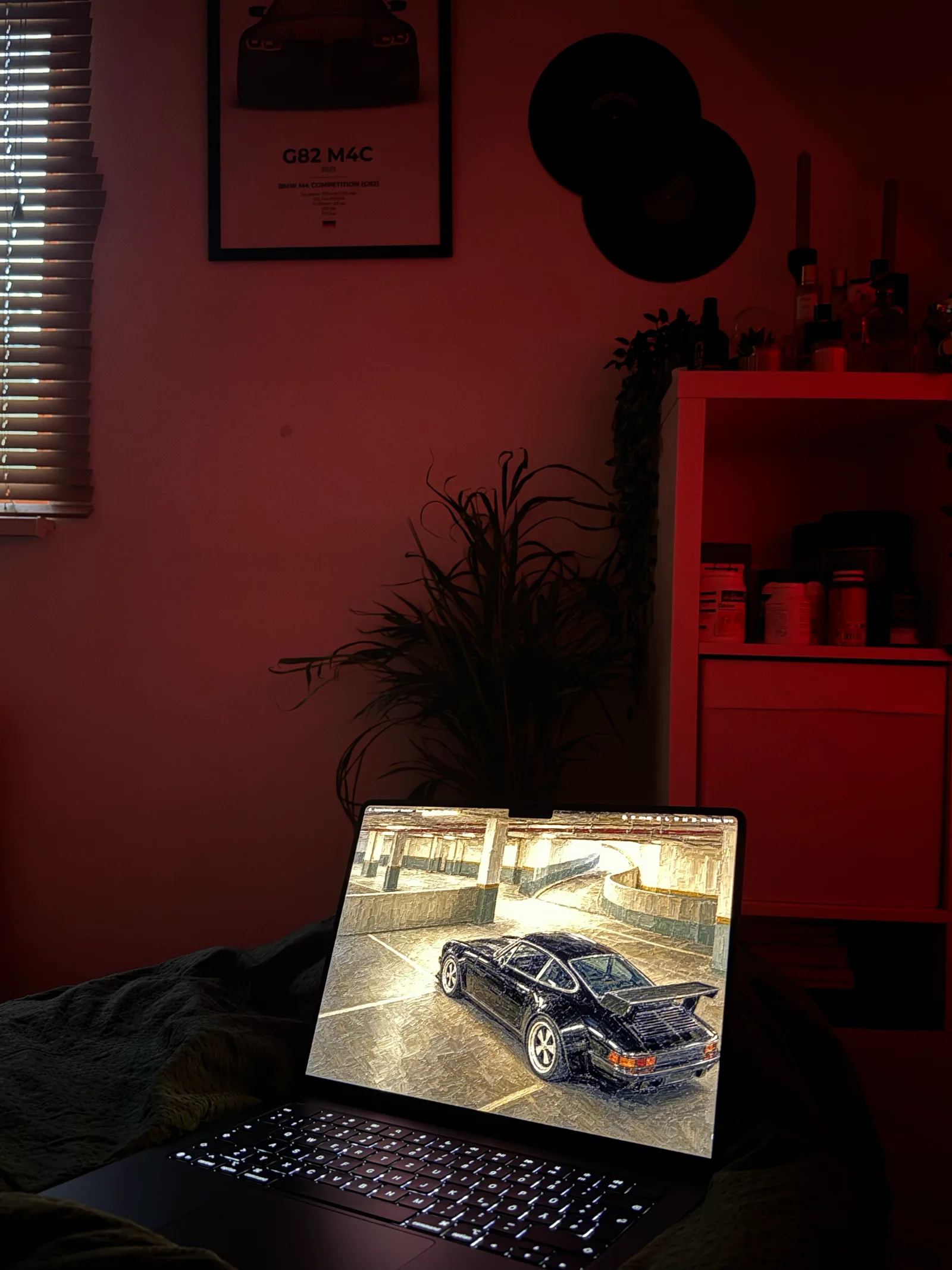 Rot beleuchtetes Zimmer mit Poster und Schallplatten, das Notebook zeigt den dunklen Porsche im Parkhaus.