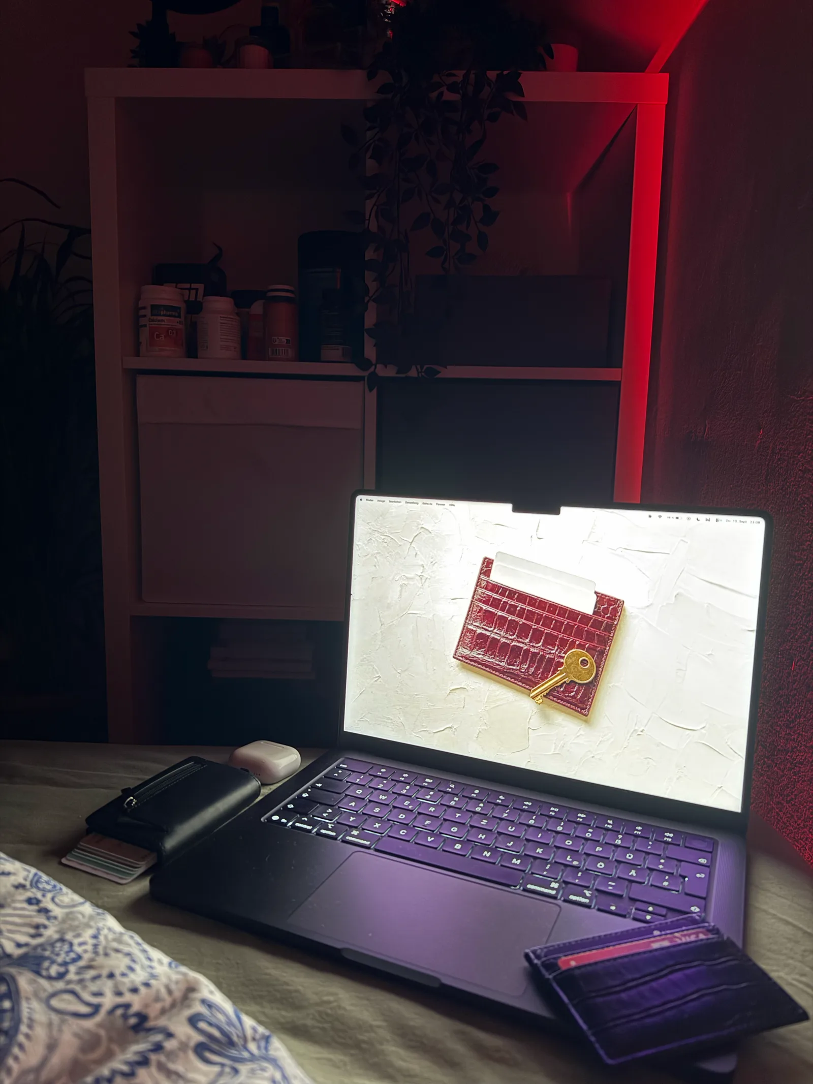 Notebook auf dem Schreibtisch vor einem Regal, auf dem Bildschirm das rote Kartenetui mit Schlüssel.