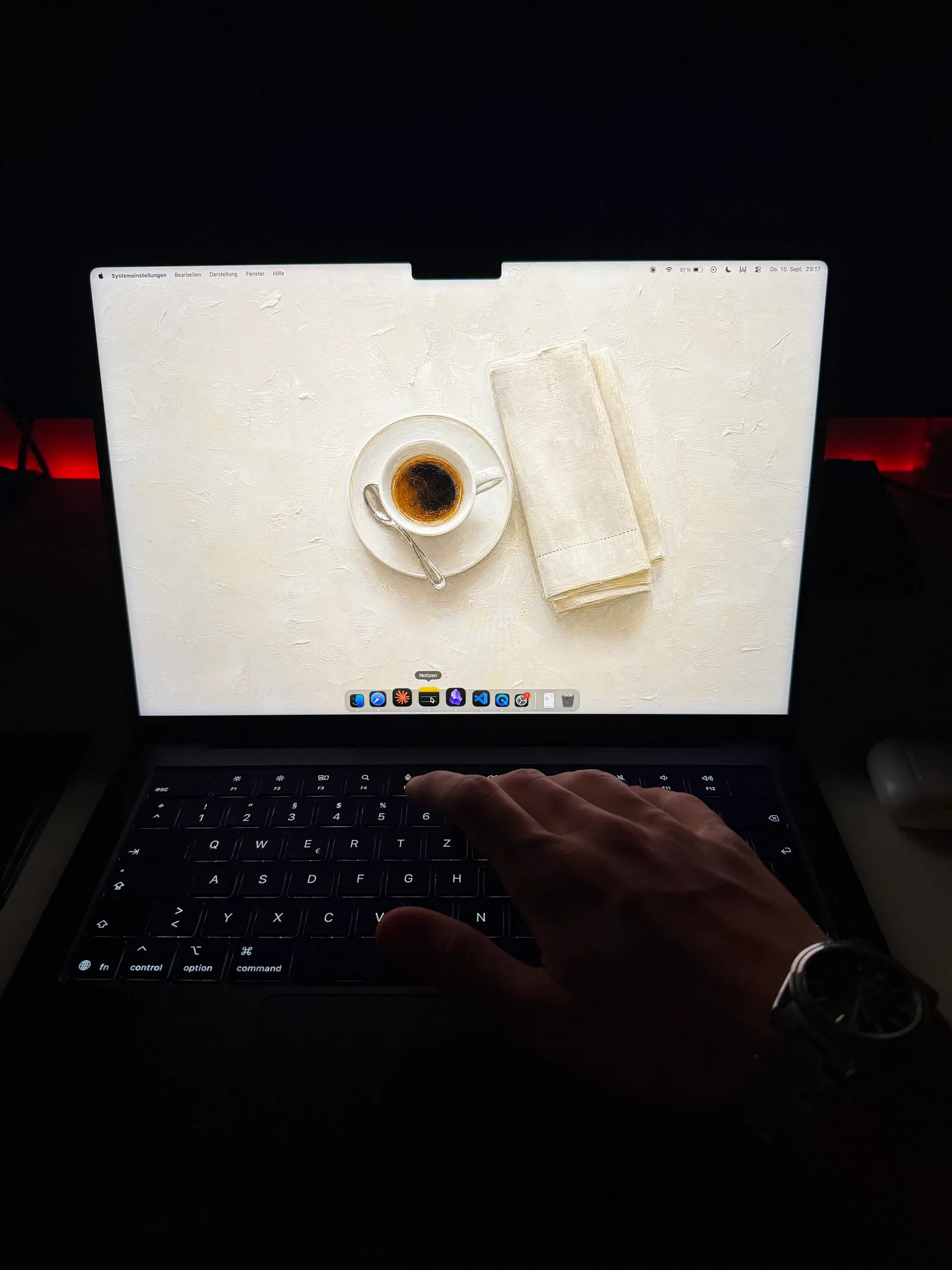 Hand auf der Tastatur im dunklen Raum, auf dem Bildschirm die Espressotasse neben der gefalteten Serviette.